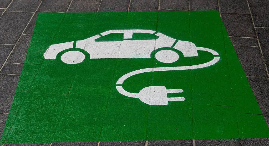 A green sign with a car plugged into a charger.