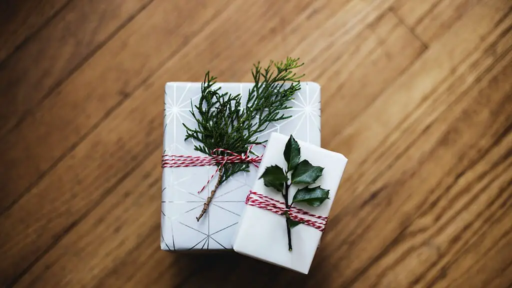 A white gift wrapped with a sprig of rosemary.
