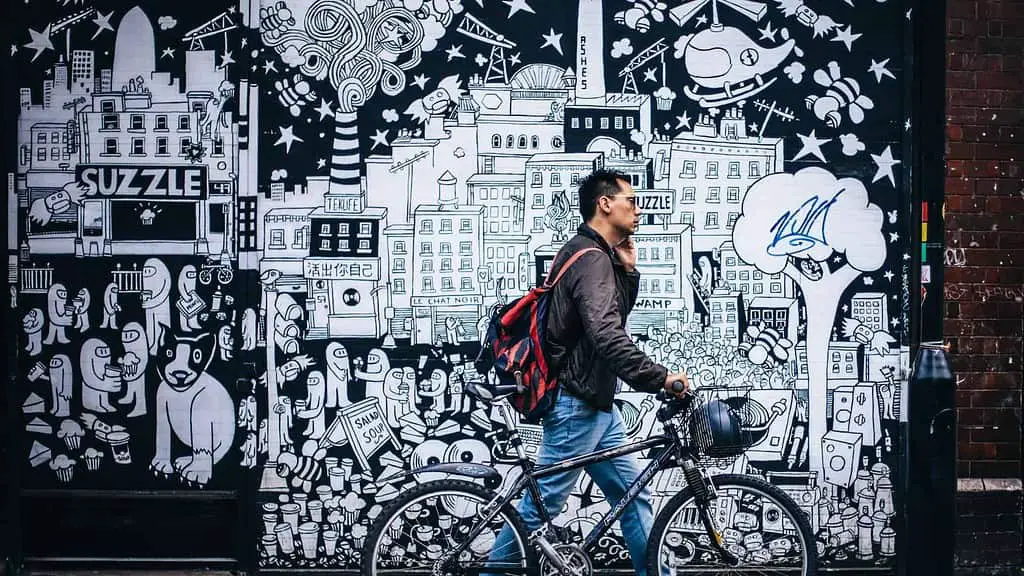 A man riding a bicycle in front of a mural.
